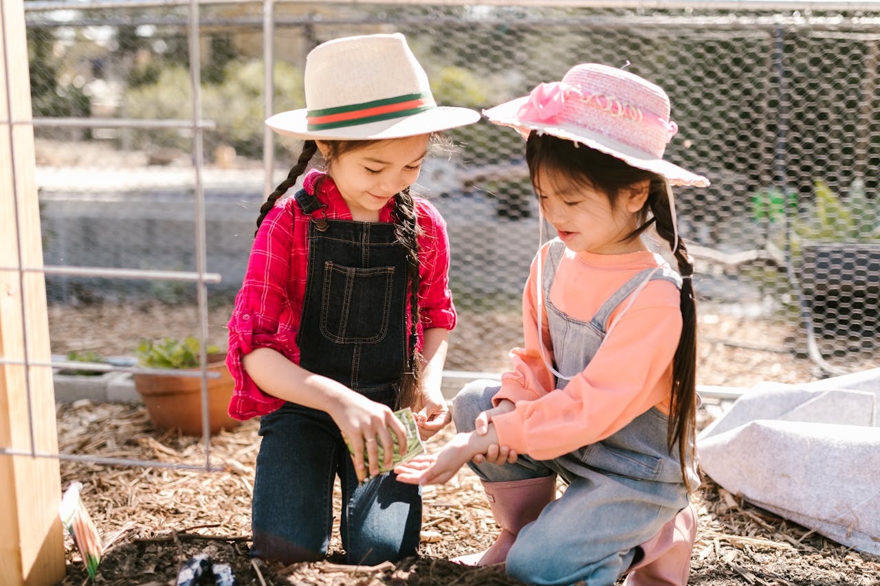Two young girls gardening together outdoors in sunny weather.